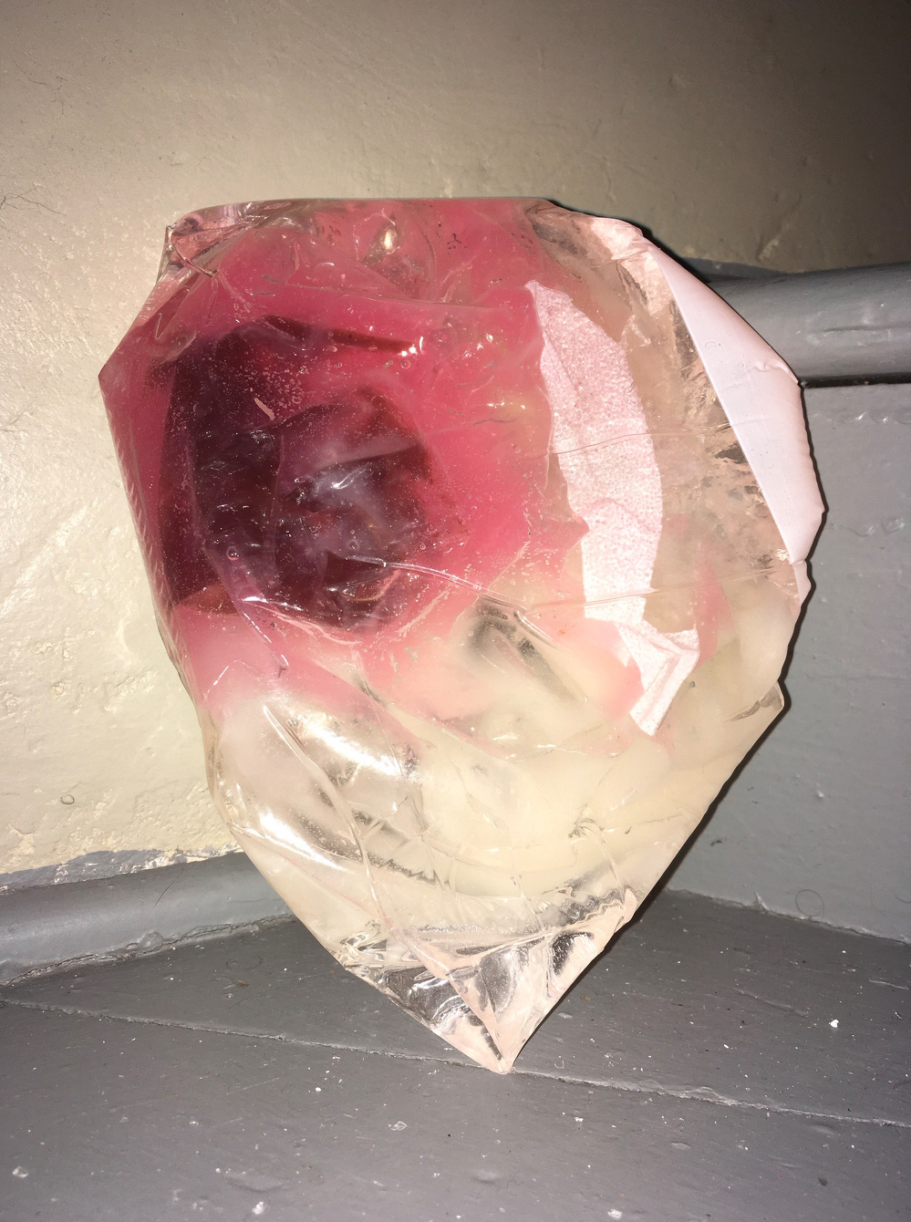 A translucent, crumpled plastic sheet with pink and clear sections is resting against a gray surface.