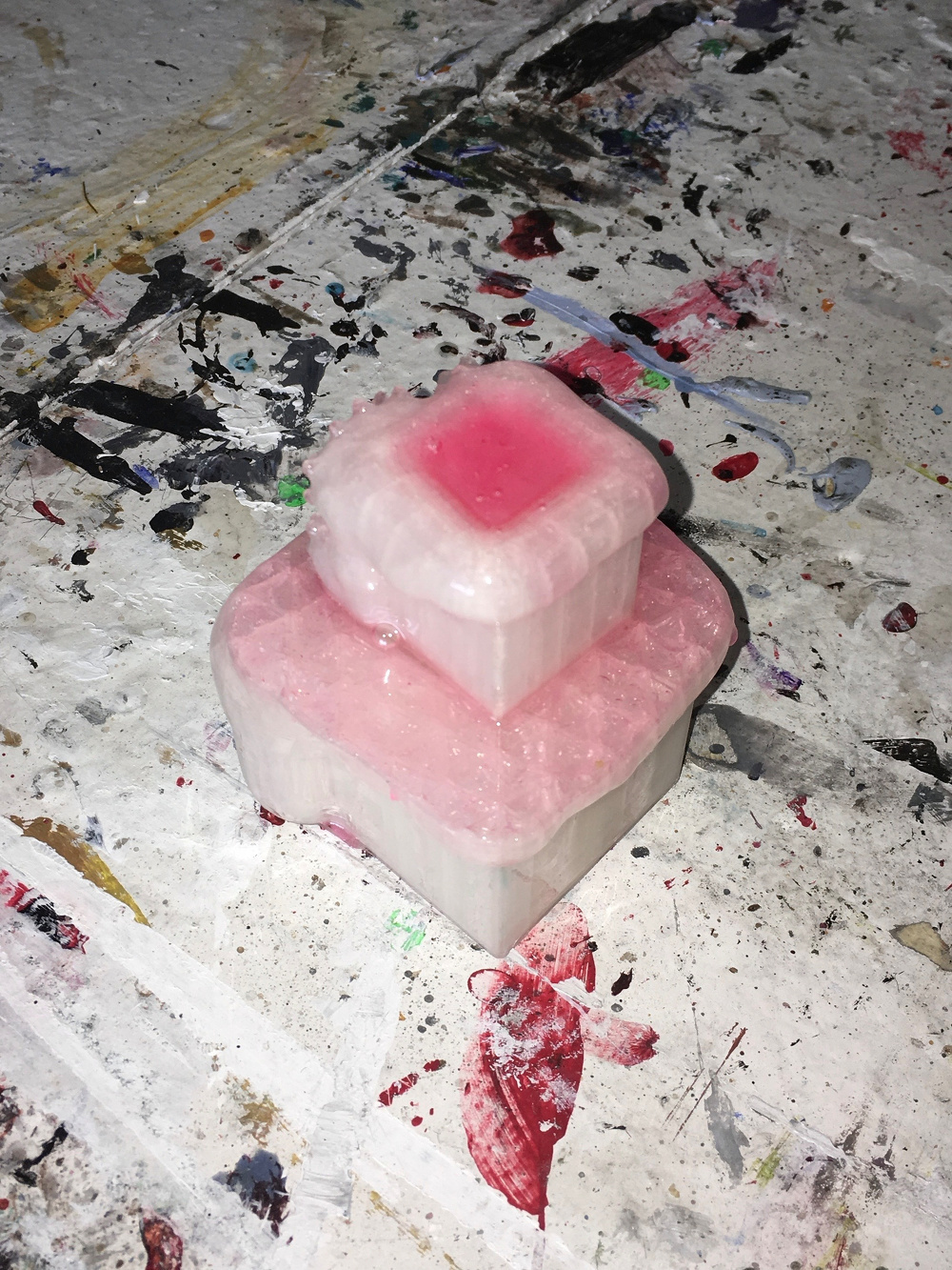 A pink, melting wax-like structure sits on a paint-splattered surface.