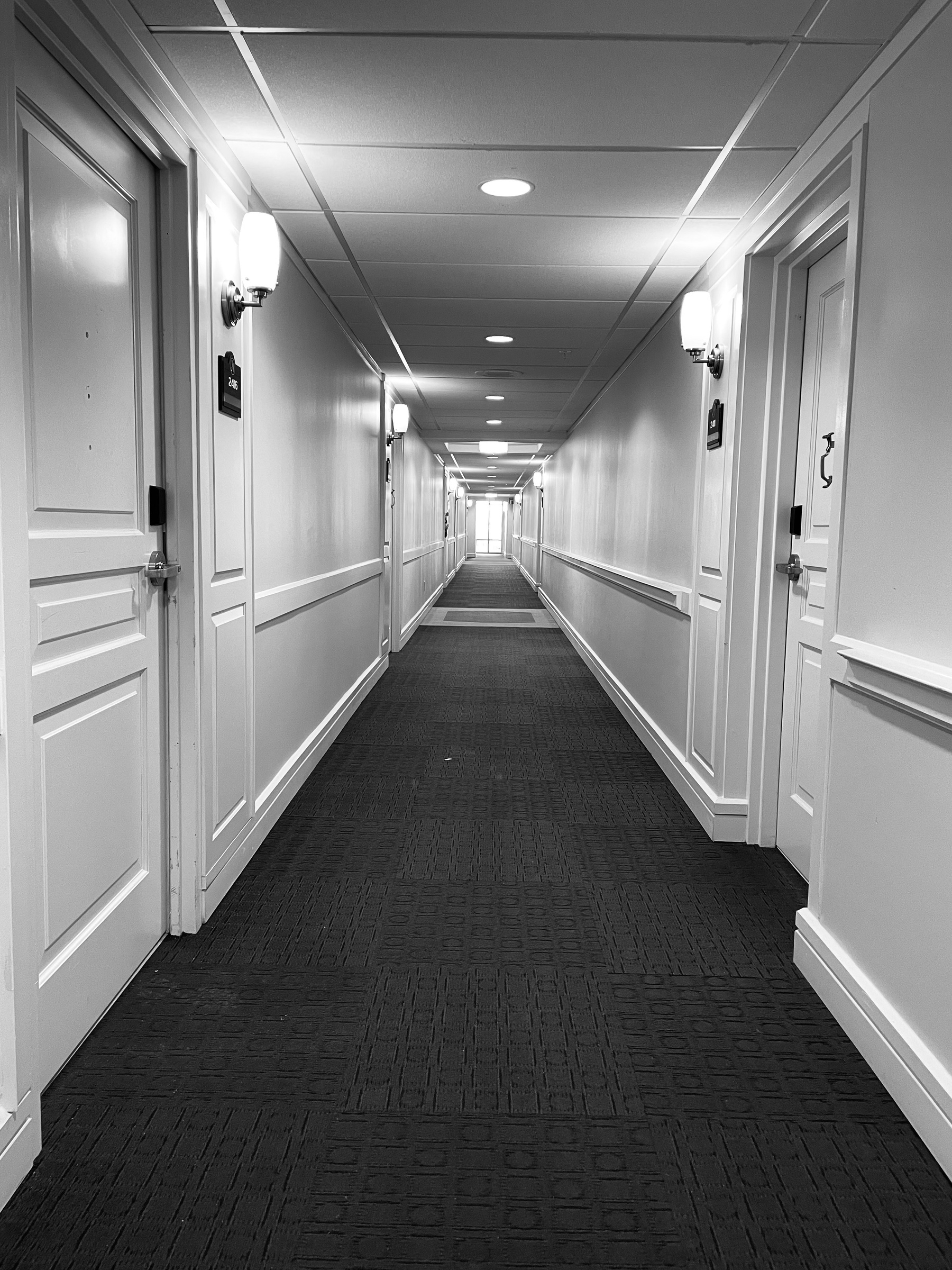 Black and white photo of a long hallway with a window at the end