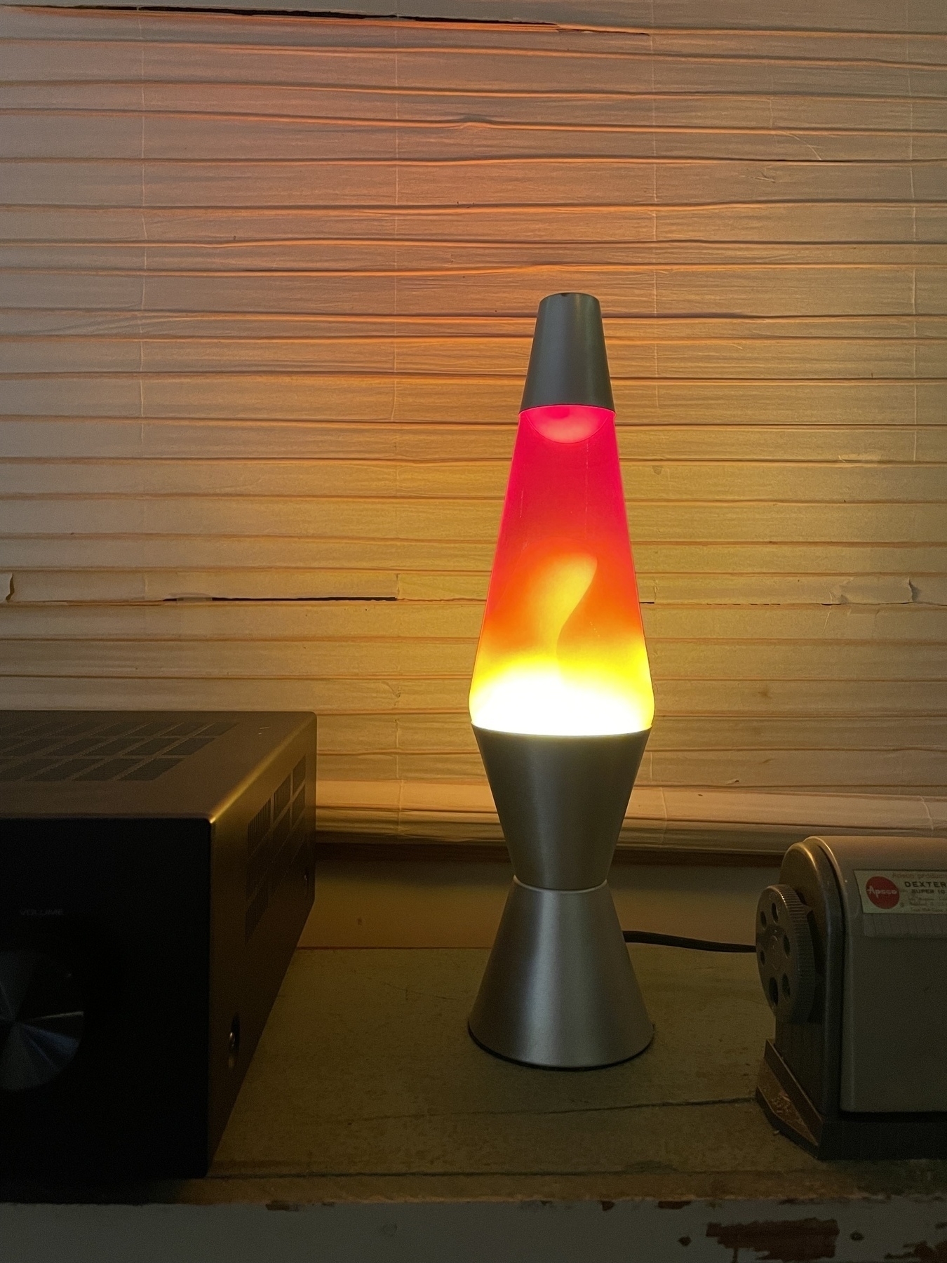 A red lava lamp an a shelf between an amplifier and a pencil sharpener