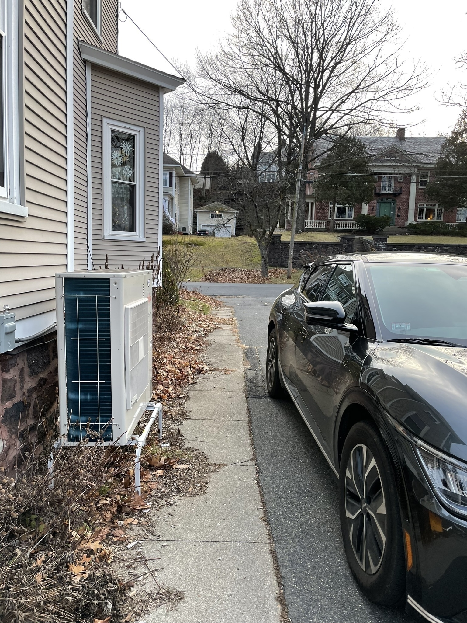 Mini split condenser next to a house and facing a car parked in the driveway