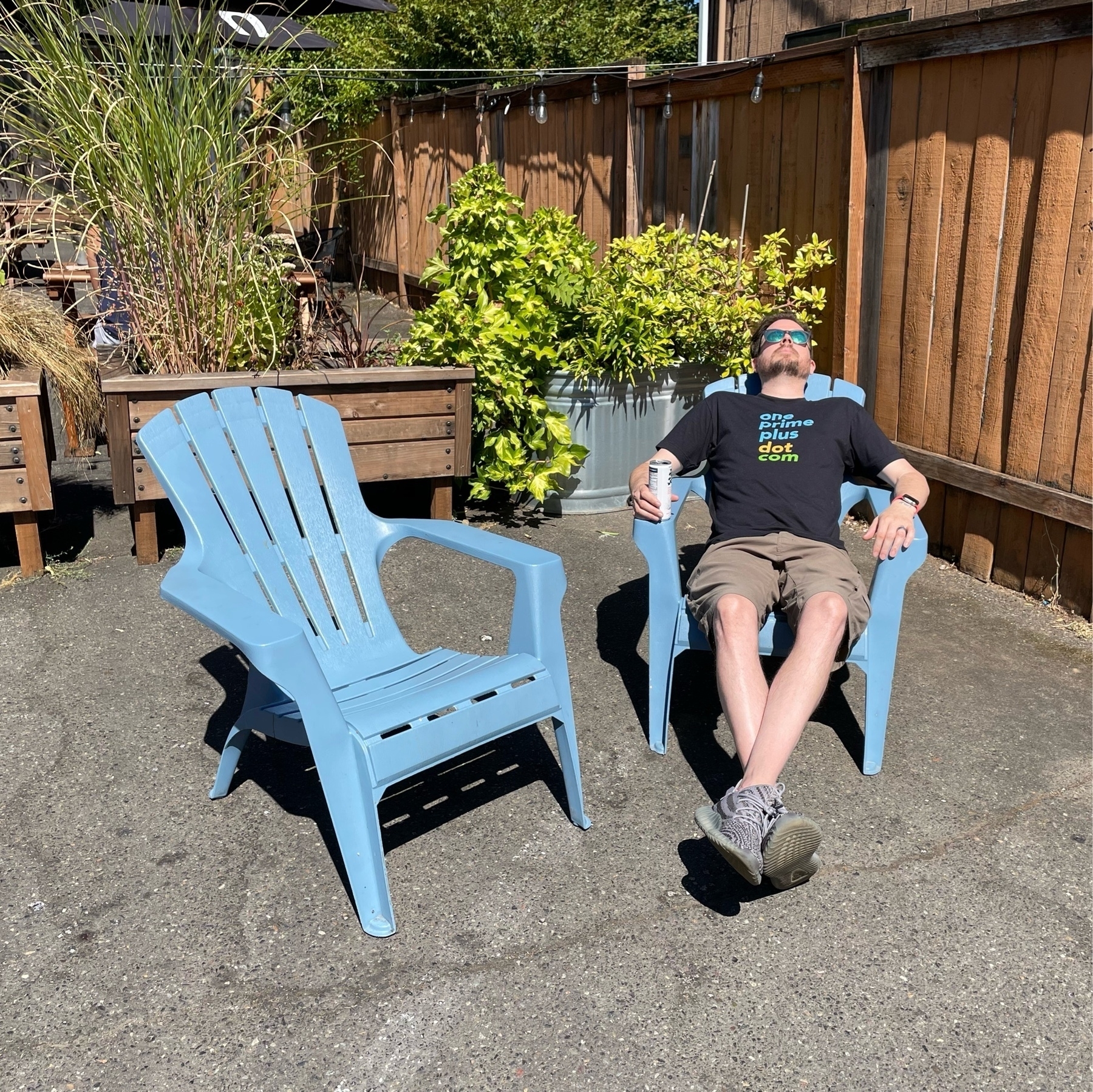 Jason sits recline in a backyard chair while having a drink and wearing sunglasses.