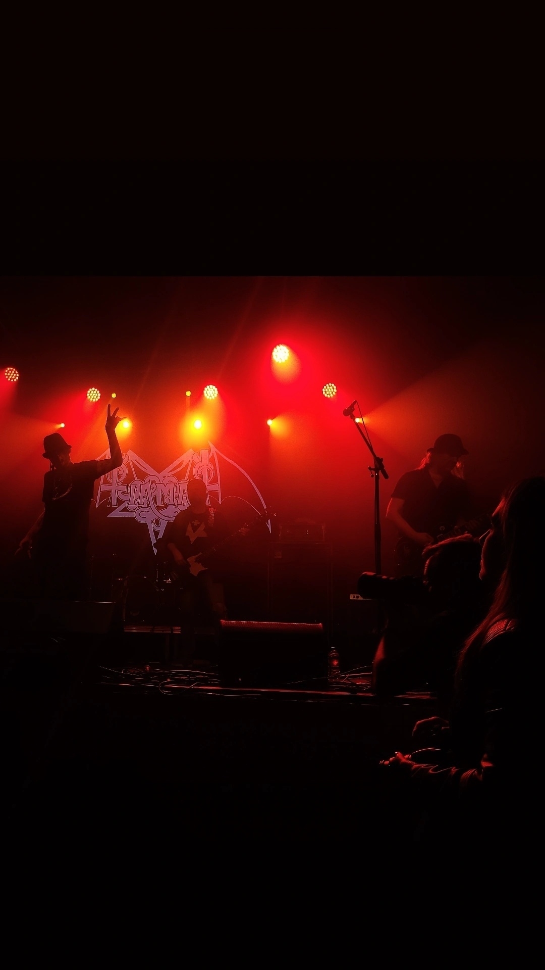 A band is performing on stage under red and orange lights with a visible logo in the background.