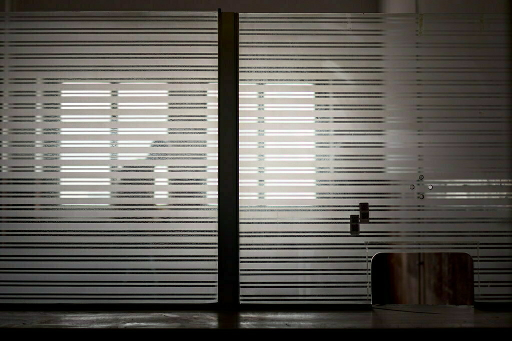 A silhouette of a person is visible behind a frosted glass partition with horizontal stripes.