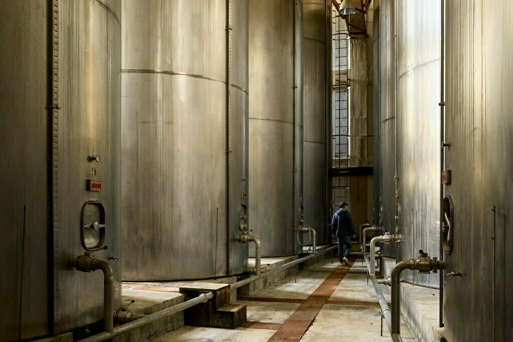 A person is walking between large industrial storage tanks in a facility.