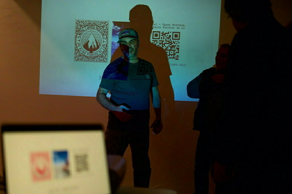 A person stands in front of a screen projecting QR codes and images, casting a shadow, with a laptop in the foreground.