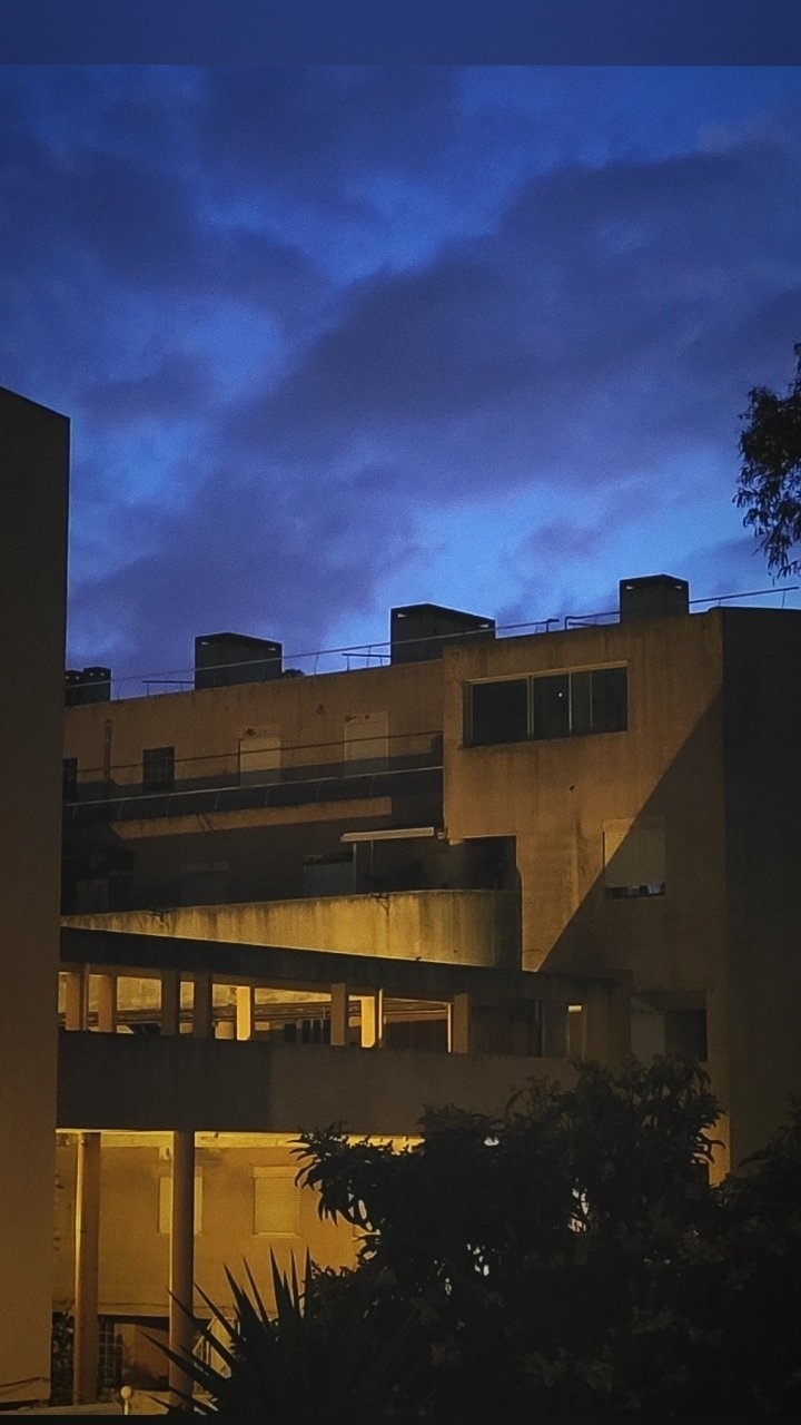 A building with illuminated passages is set against a backdrop of a deep blue evening sky.