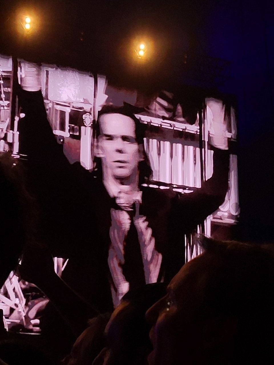 A performer on a large screen engages a crowd at a concert, surrounded by dramatic lighting.