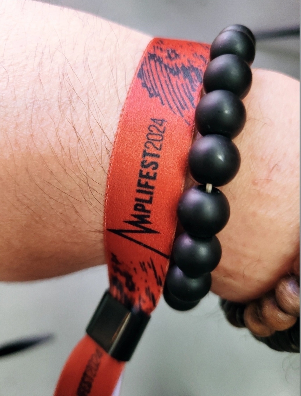 A red festival wristband with "AMPLIFEST 2024" printed on it is worn alongside a black beaded bracelet.