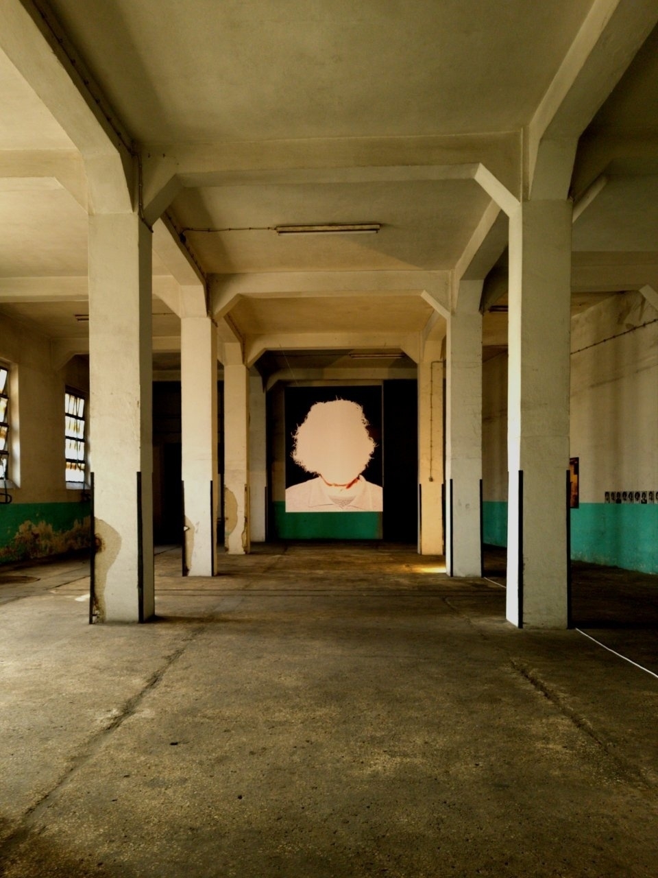 A large, empty industrial room features a prominent artwork of a face with an unclear identity on the far wall.