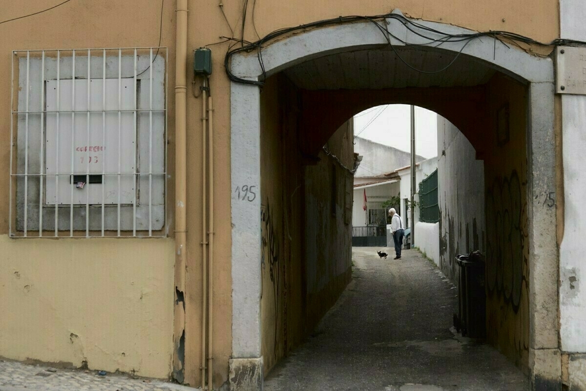 Auto-generated description: A narrow archway leads to an alley where a person is walking a small dog.