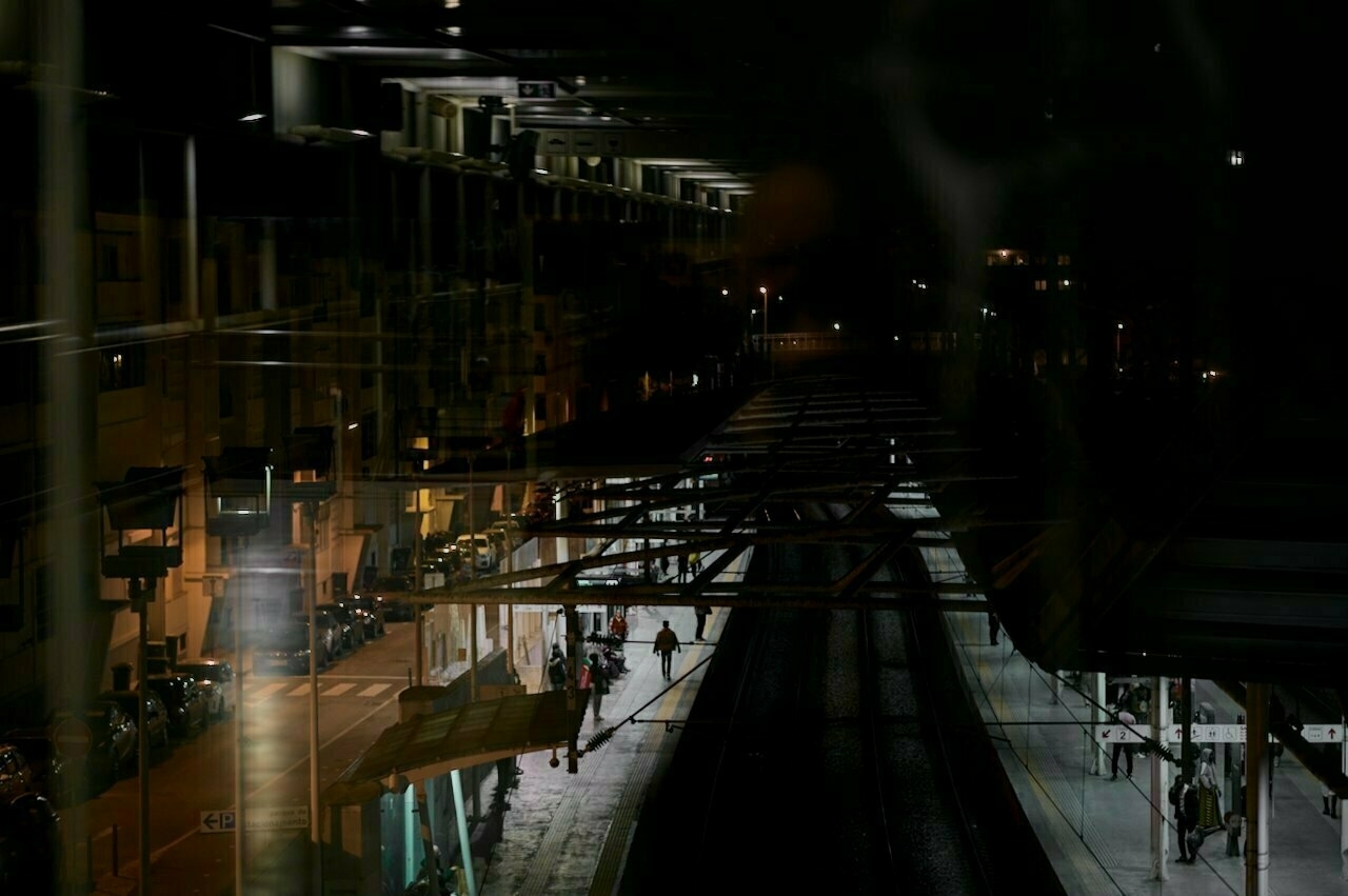 A dark urban railway station is captured at night with reflections creating an abstract effect.