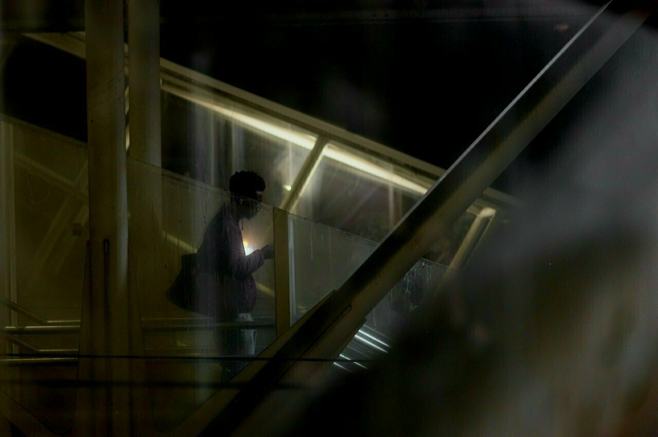 A person holding a phone ascends a dimly lit staircase at night.