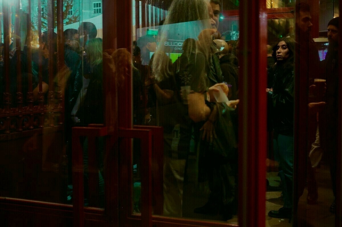 A group of people is gathered indoors, seen through a reflective glass door.