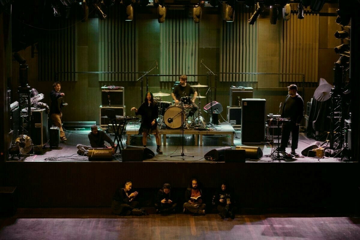 A band is setting up on stage with various musical instruments while a group of people sits in front of the stage.