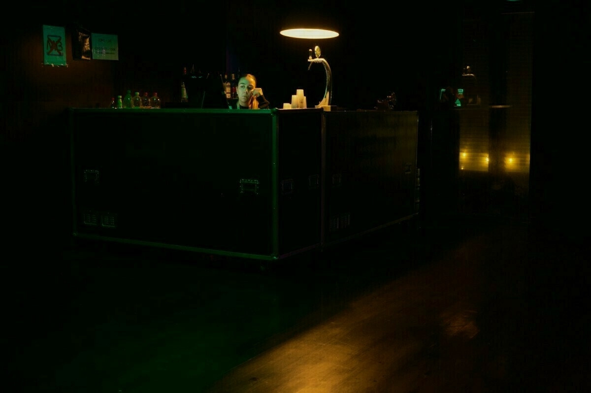 A dimly lit bar with a person sitting at a counter under a lamp.