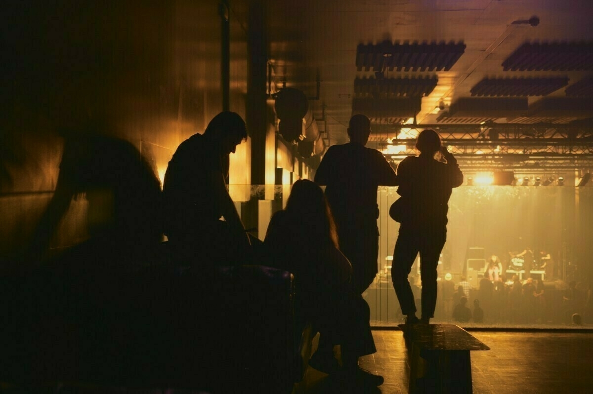 A group of people is silhouetted against a dimly lit concert venue, creating a dramatic and atmospheric scene.