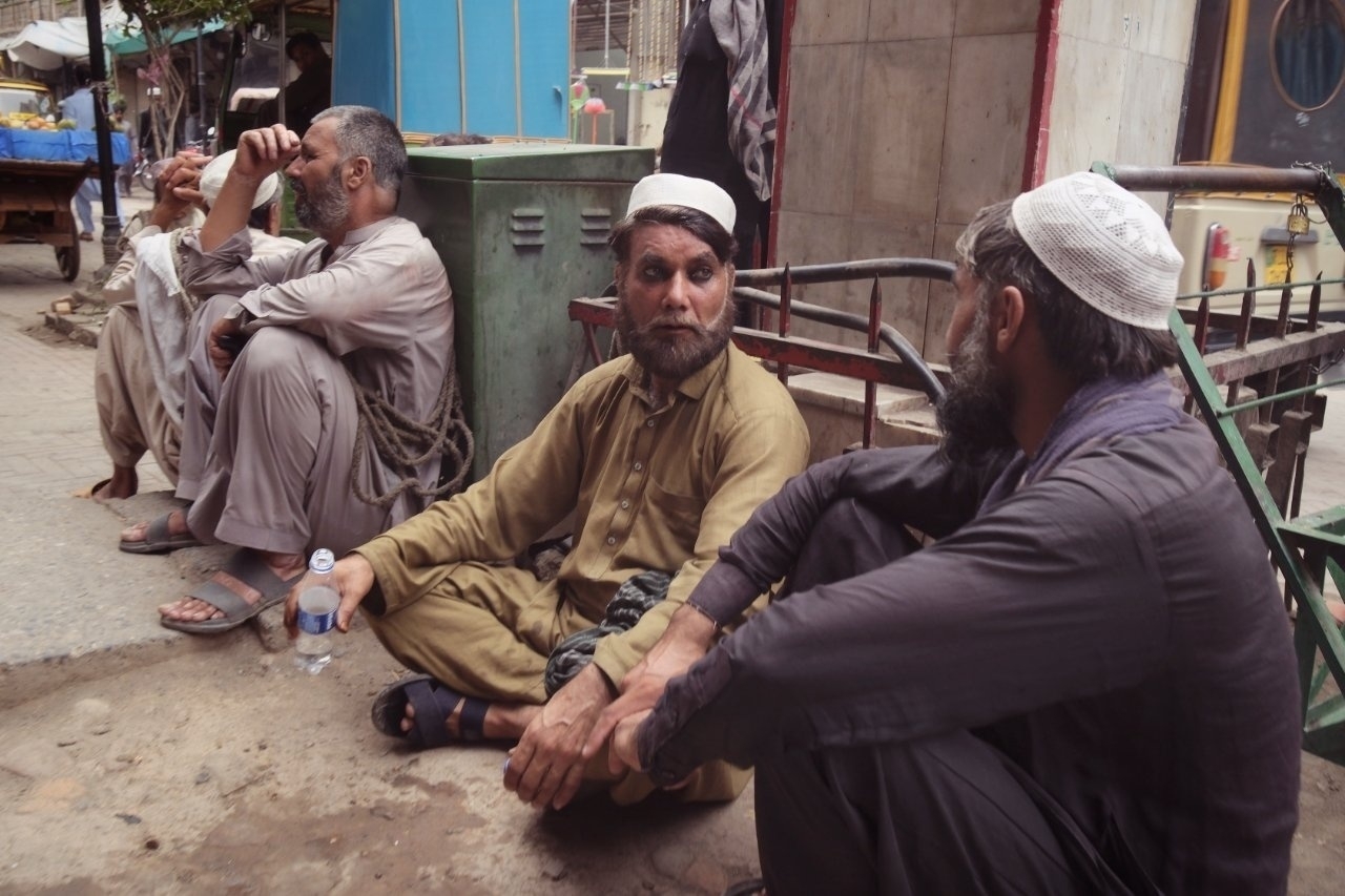 A group of men wearing traditional clothing is sitting and talking on a street sidewalk.
