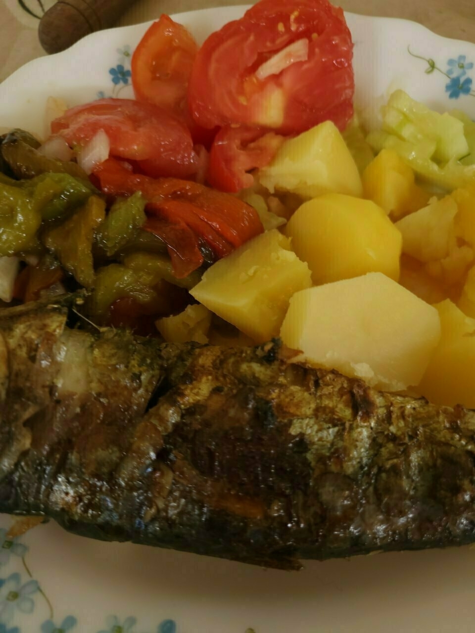 A plate of food featuring a grilled fish, boiled potatoes, and a colorful mix of fresh tomatoes and vegetables.