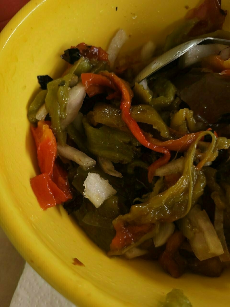 A bowl contains a colorful mix of roasted peppers and chopped onions with a metal spoon.