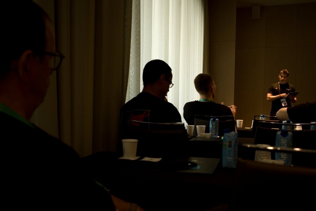 A person is speaking to an audience in a dimly lit room with people sitting at tables.