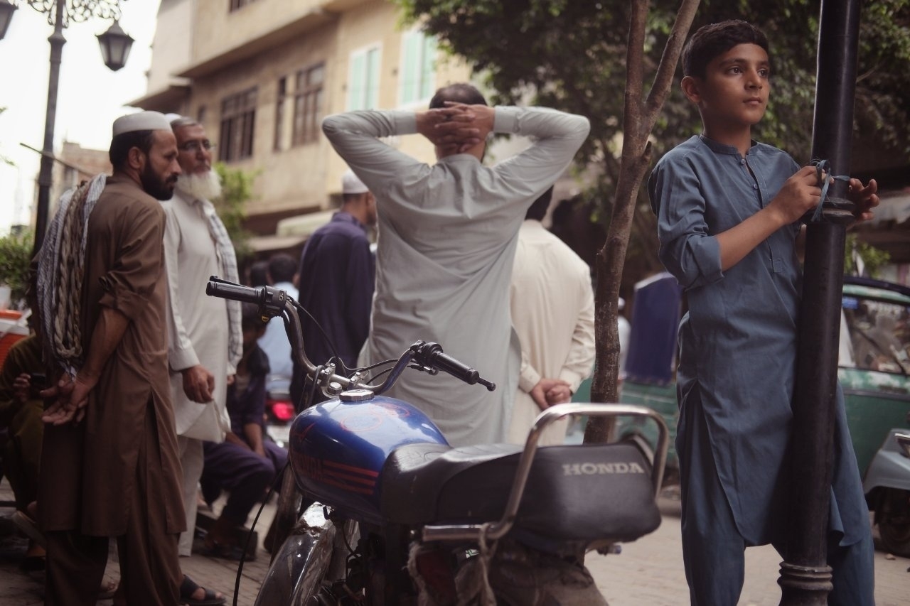 A group of men and a boy in traditional clothing are gathered near a parked motorcycle on a street.