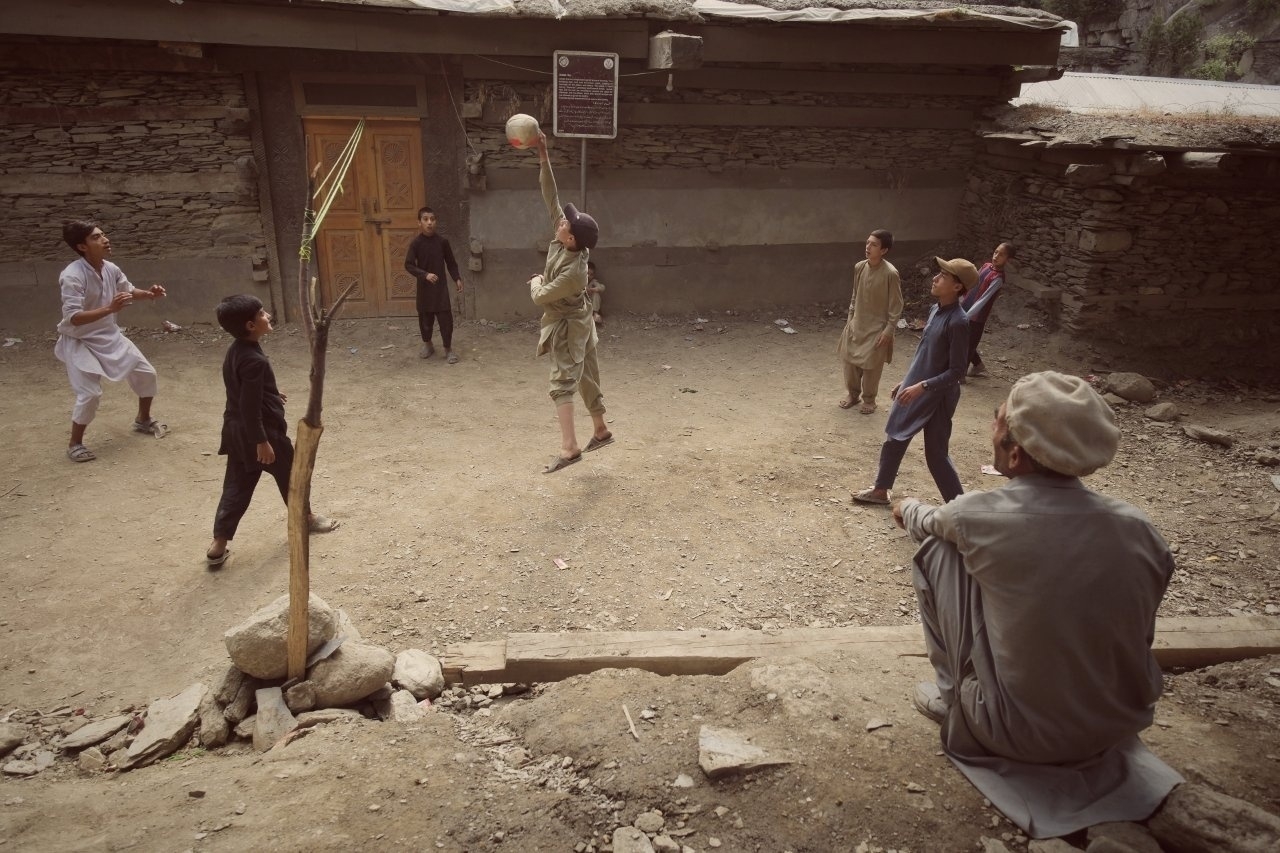 A group of children is playing with a ball in a courtyard while an older person watches them.