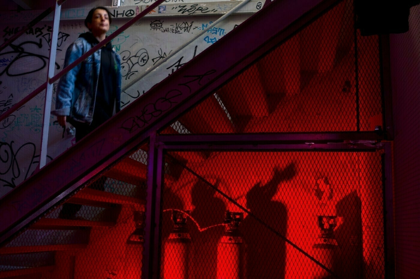 A person walks down a graffiti-covered stairwell illuminated by red lighting.