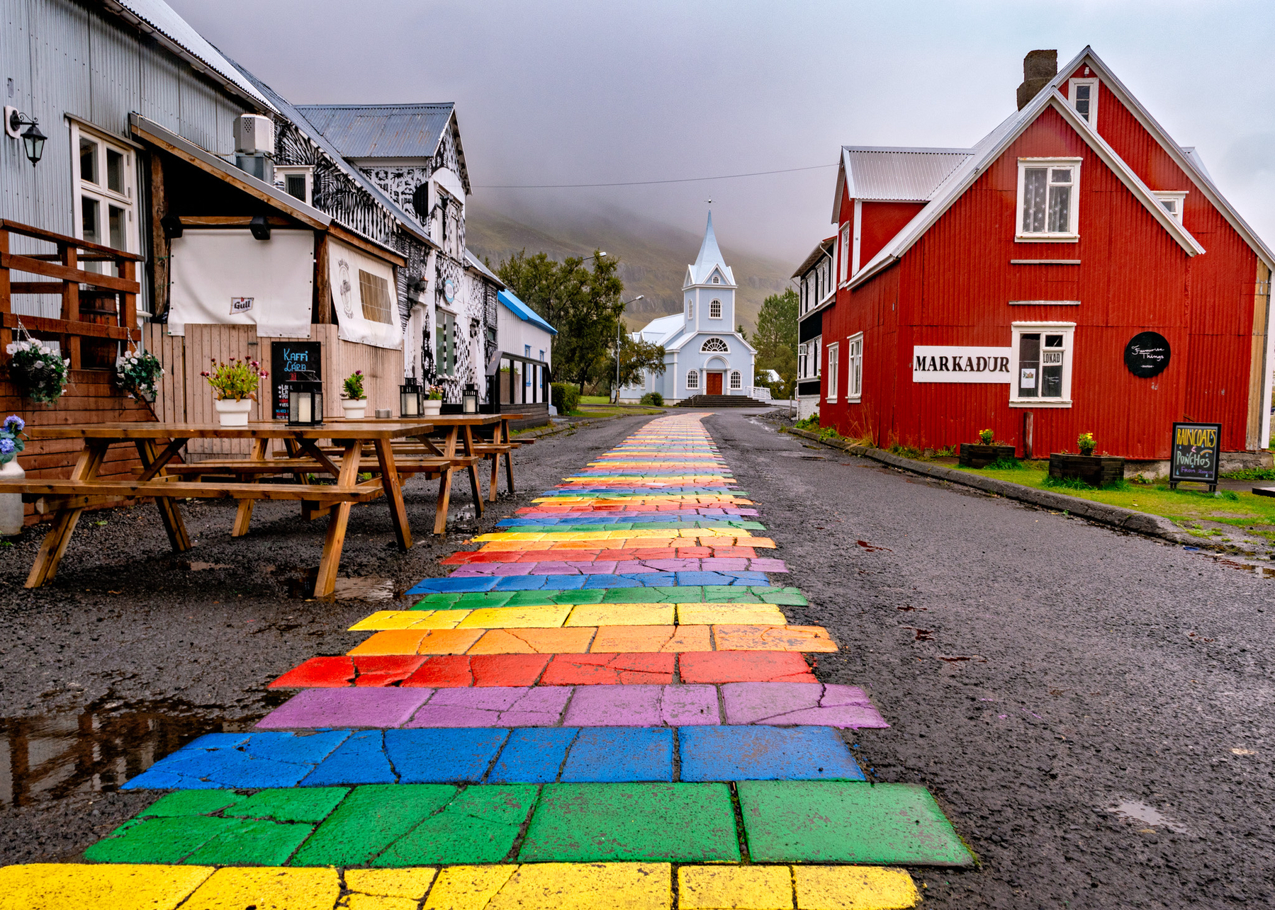 Image of the main street of Seydisfjordur, Iceland, with a rainbow pattern leading towards the church past a few shops.
