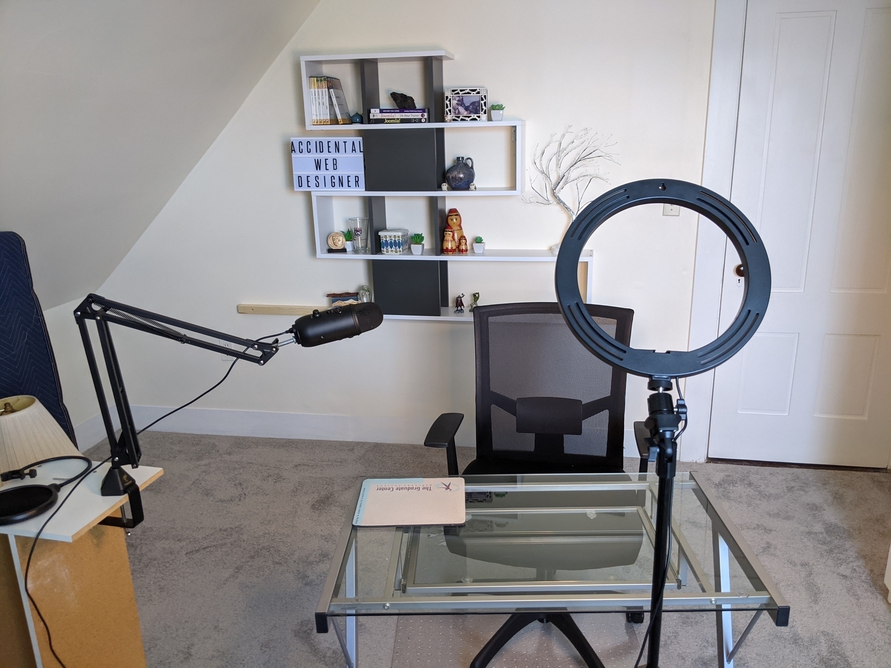 Photo of shelf on the wall, glass desk and chair, microphone on a boom.