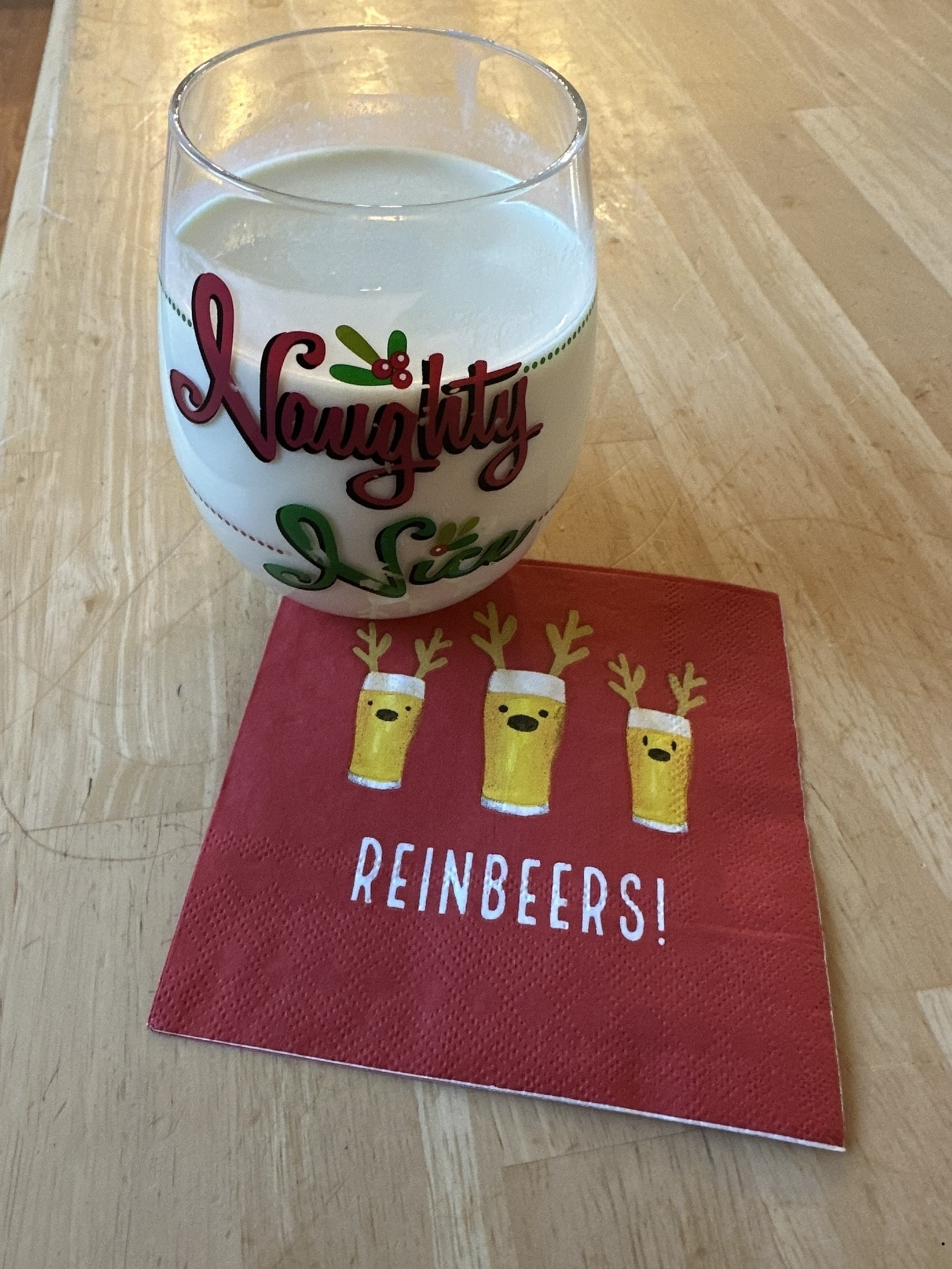 Egg nog in a glass saying “naughty nice” on a napkin with cartoon glasses of beer with antlers and the text “Reinbeers”