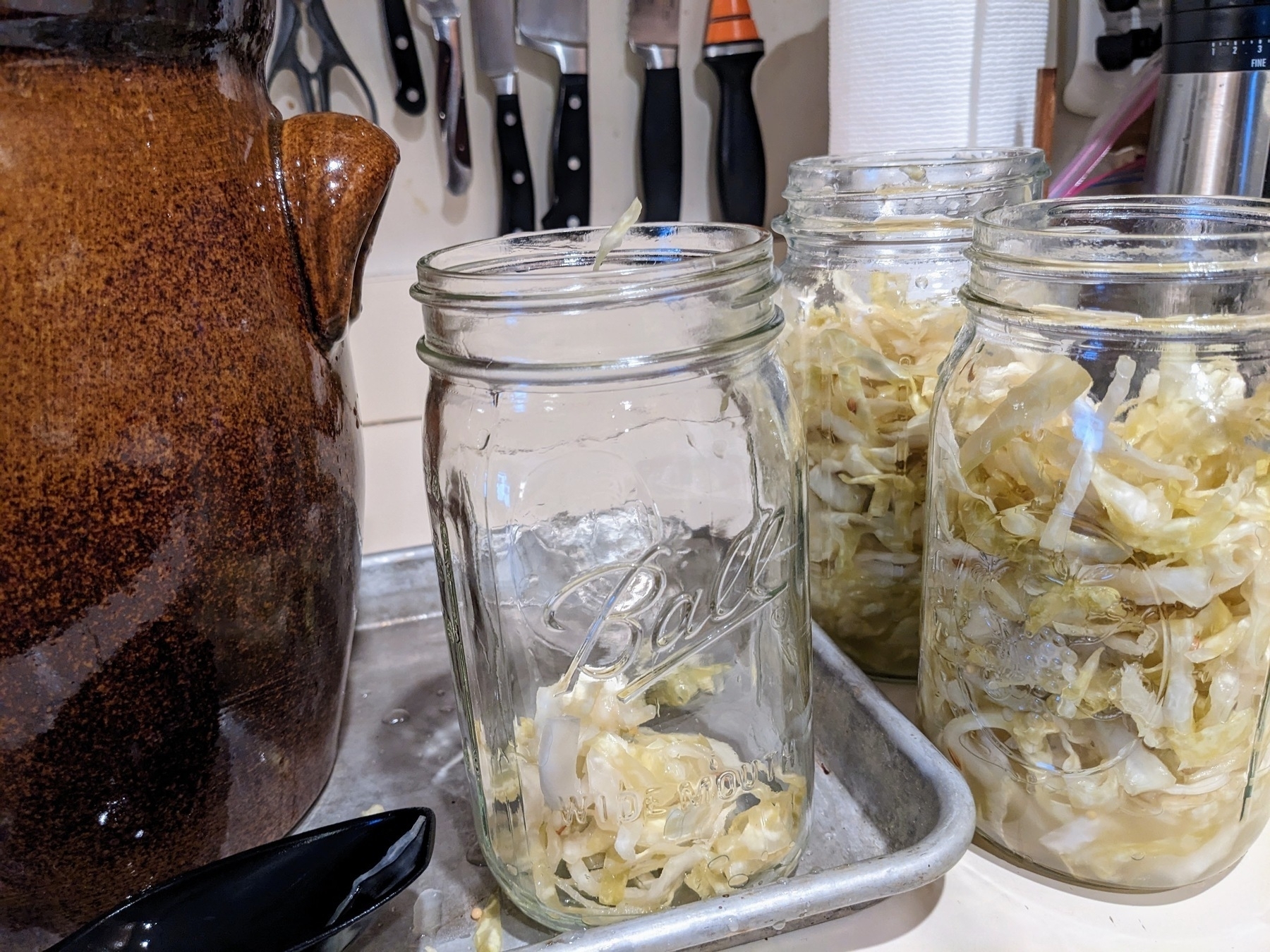 three jars of sauerkraut next to a fermenting crock