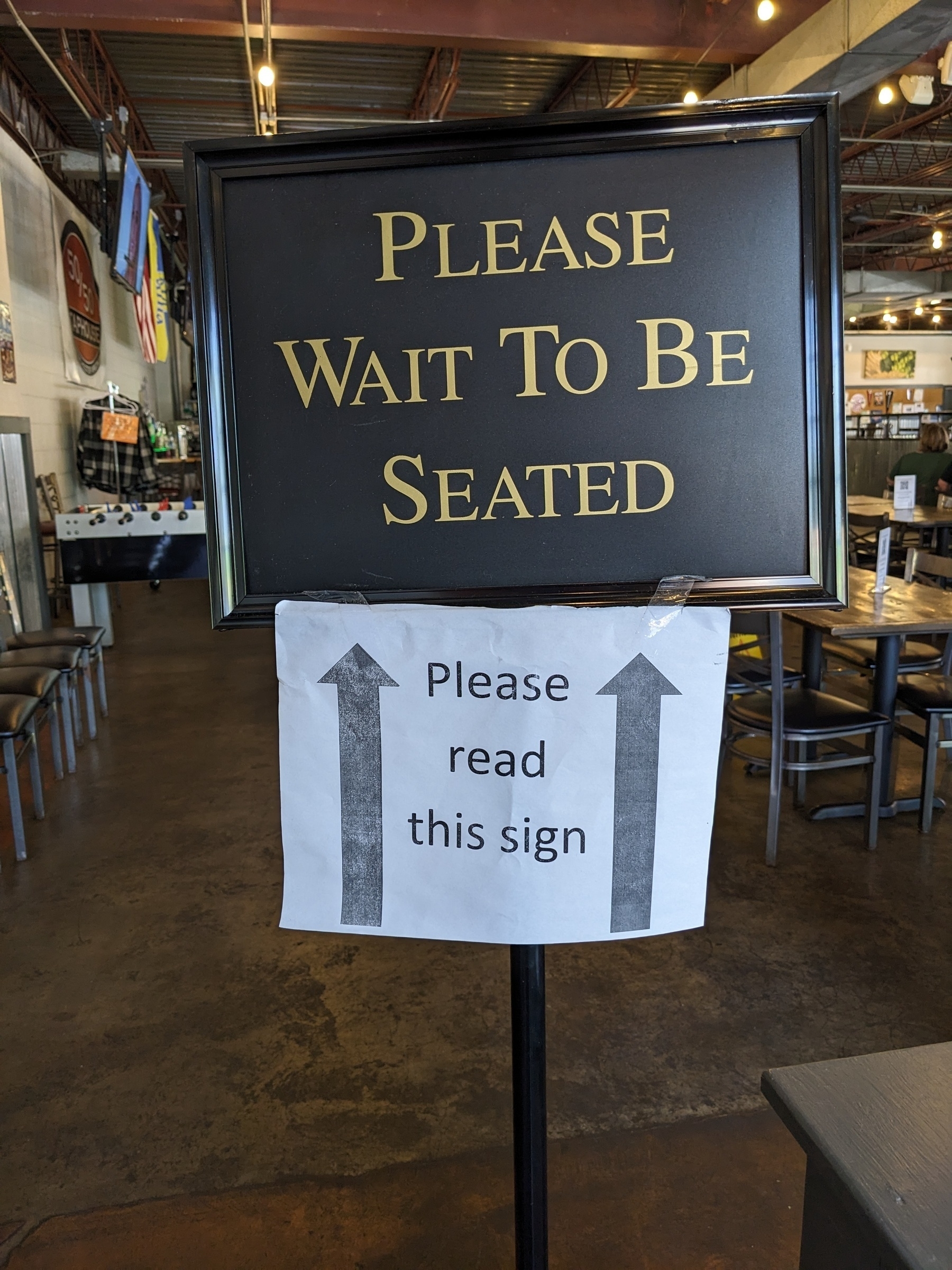 Commercial restaurant sign that says, 'Please wait to be seated,' with printed sign tape underneath that says, 'Please read this sign' 