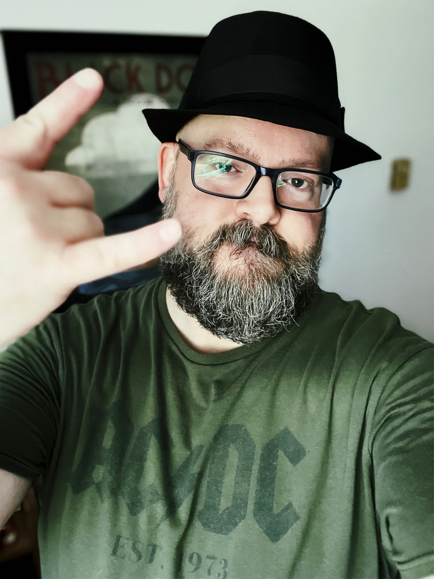 Portrait of me in a forest green tee with the AC/DC band logo on it. I’m wearing my black Trilby (of course), and giving the “rock on” hand gesture. With luck, I look like a cool geek instead of just a geek.