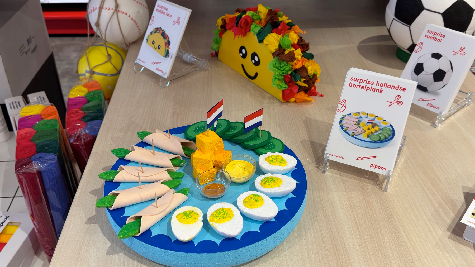 Auto-generated description: A display showcases colorful, play food items shaped like traditional Dutch dishes, with various toys and decorations inspired by sports and food themes.