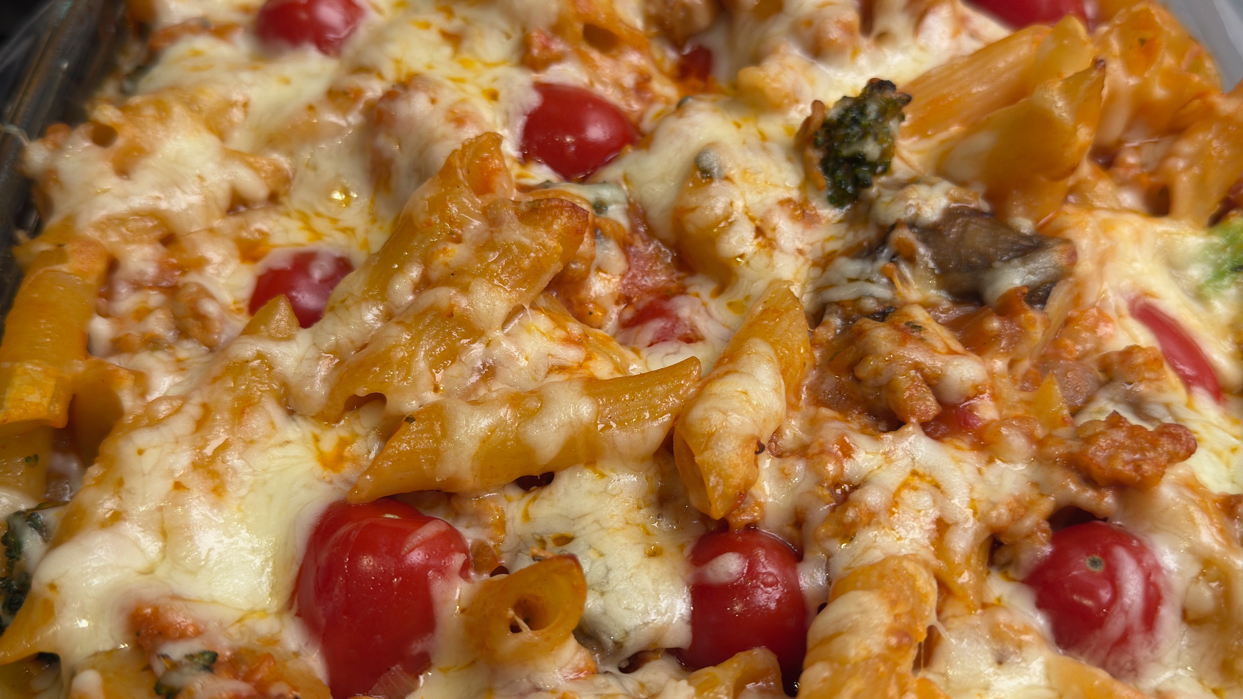 Auto-generated description: A close-up view of cheesy baked pasta with cherry tomatoes and vegetables.
