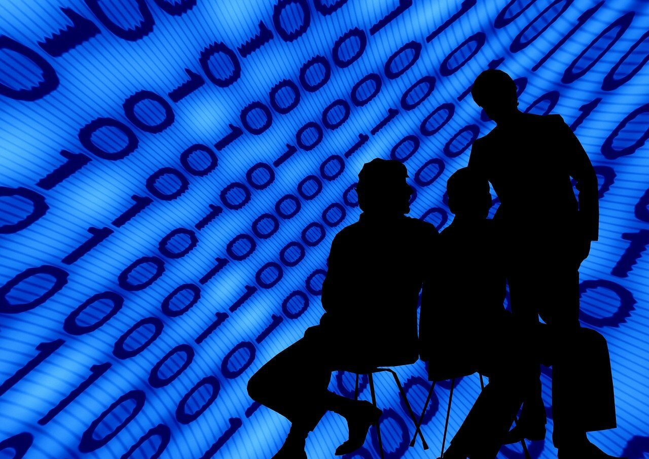 Silhouettes of three people are sitting in front of a blue digital binary code background. From geralt.