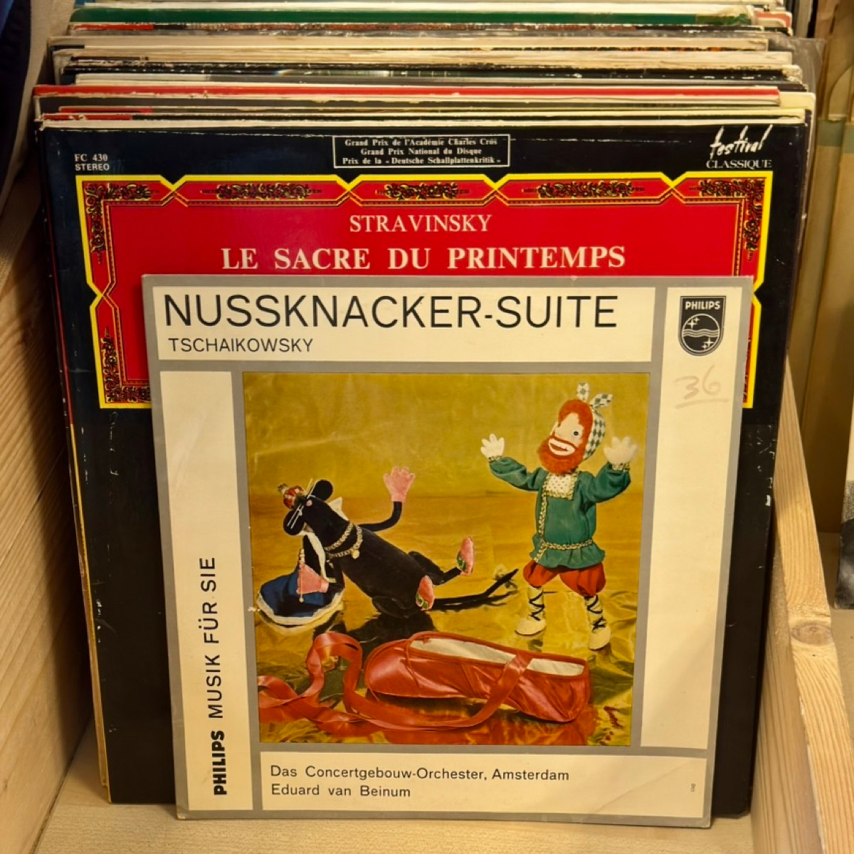 Two records leaning in a bin: a red-and-yellow Festival Classique sleeve of Stravinsky's Le Sacre du Printemps behind a Philips 'Musik für Sie' sleeve of Tchaikovsky's Nussknacker-Suite with a puppet mouse and toy soldier on the cover.