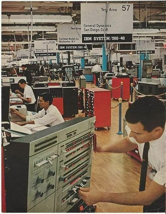 A group of people operates and manages large IBM System/360 computers in a retro-style technology facility.