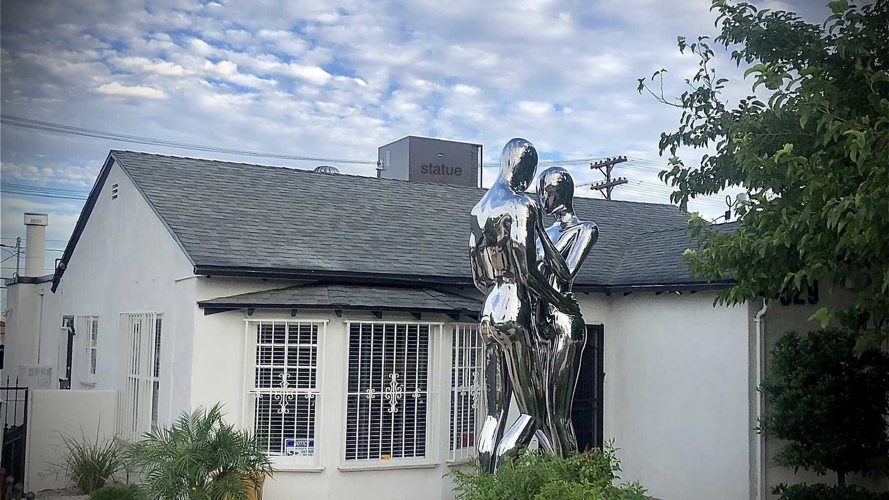 Chrome statue of two large human figures in front of a suburban home. 