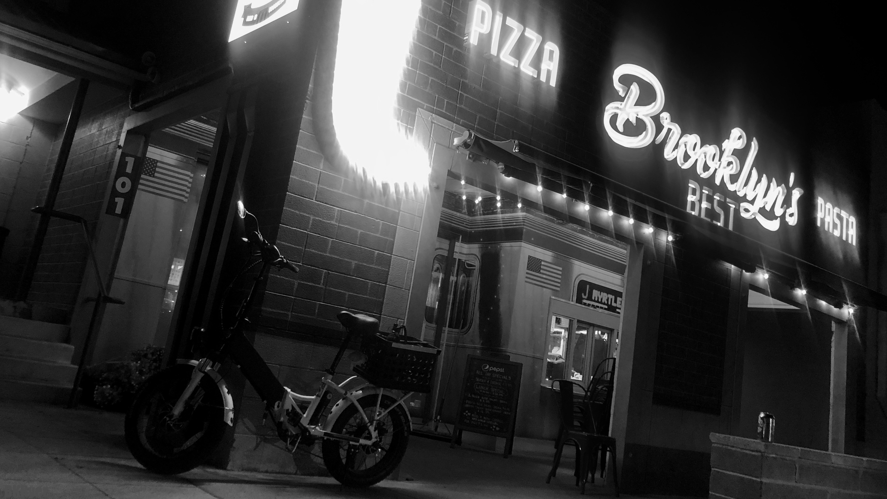 Brooklyn’s Best - Pizza restaurant with large neon sign and e-bike. 