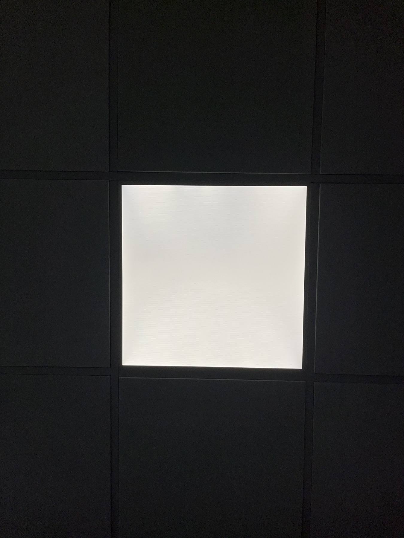 Looking straight up at a square ceiling light in a square tiled office ceiling. 