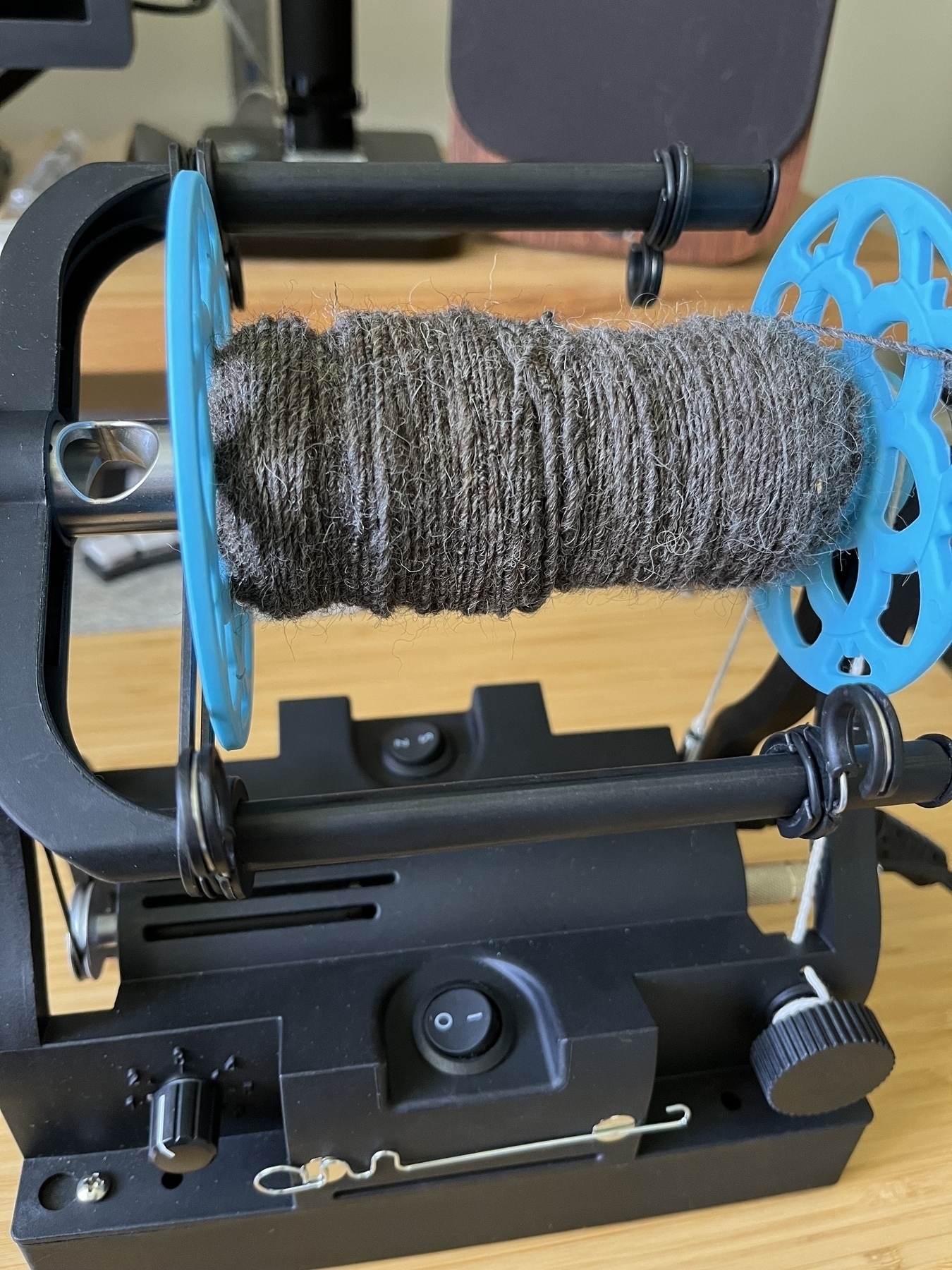 A blue e-spinner bobbin with a good covering of mid-grey hand spun yarn. 