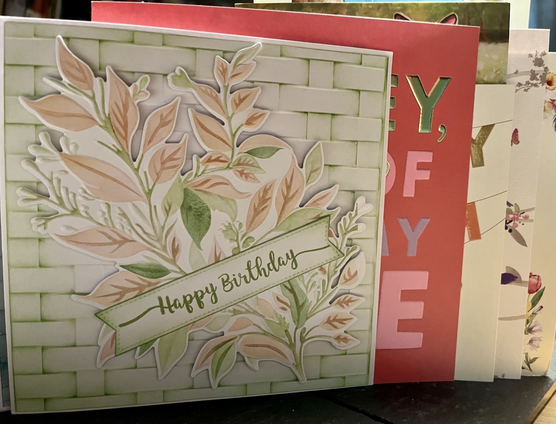 A stack of birthday cards nested into each other. The card on top is homemade by my Mum, with flowers and leaves against a basketweave background, in tones of pink and pale green. 