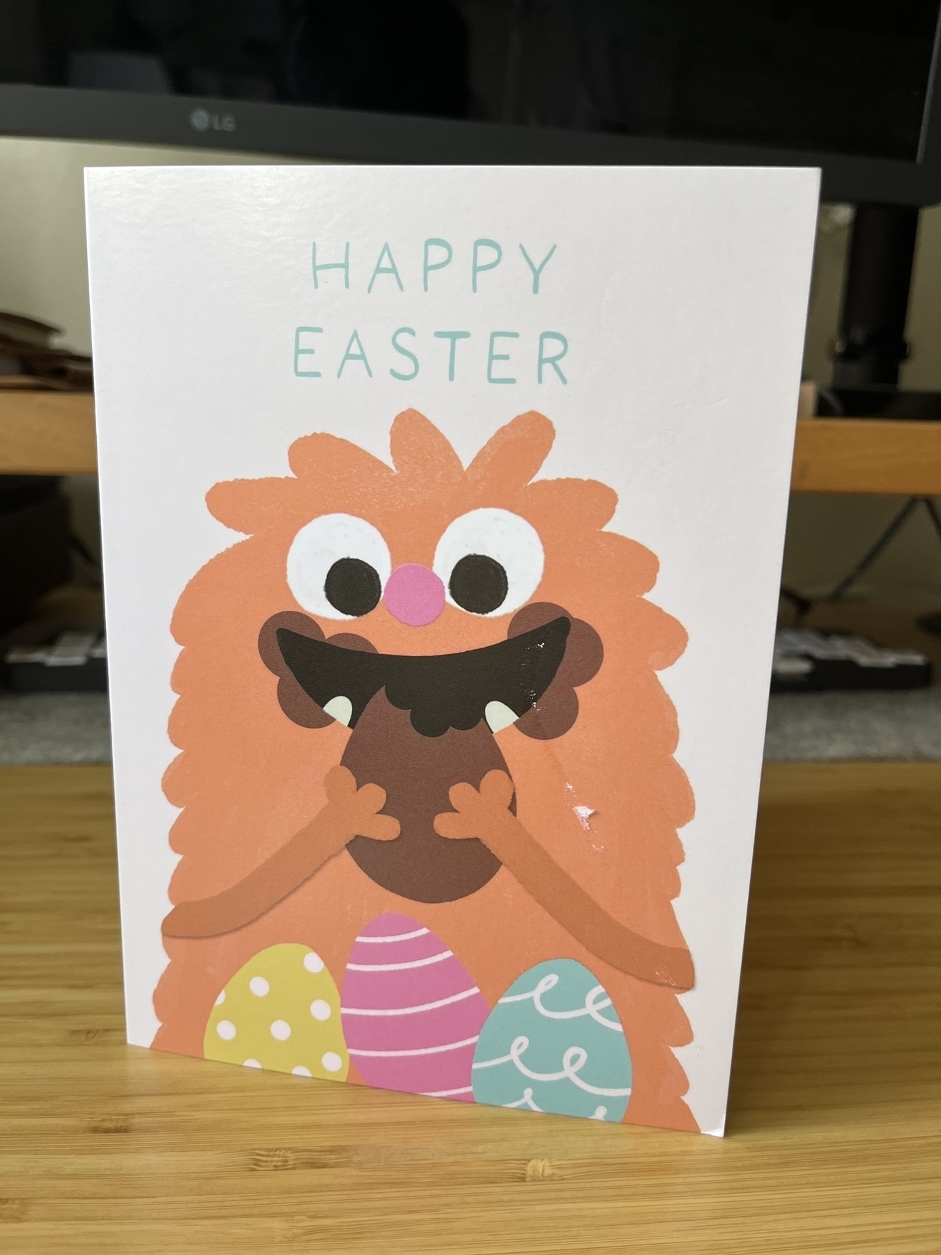 An Easter card with an illustration of a happy, hairy orange monster eating chocolate Easter eggs, with chocolate all around their mouth. 
