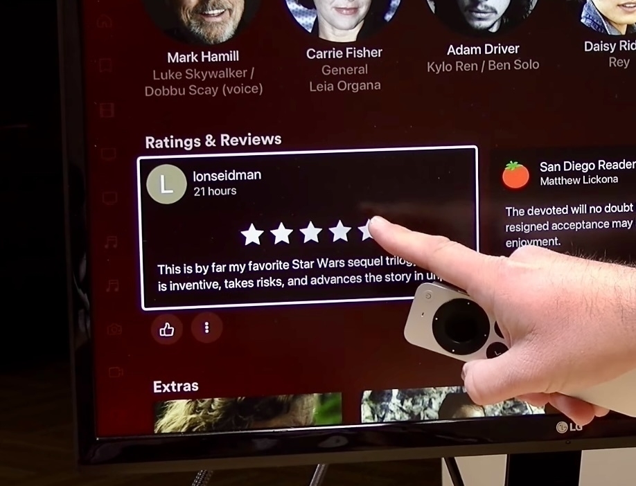 A hand holding a game controller is pointing at a five-star review on a TV screen displaying movie-related content.