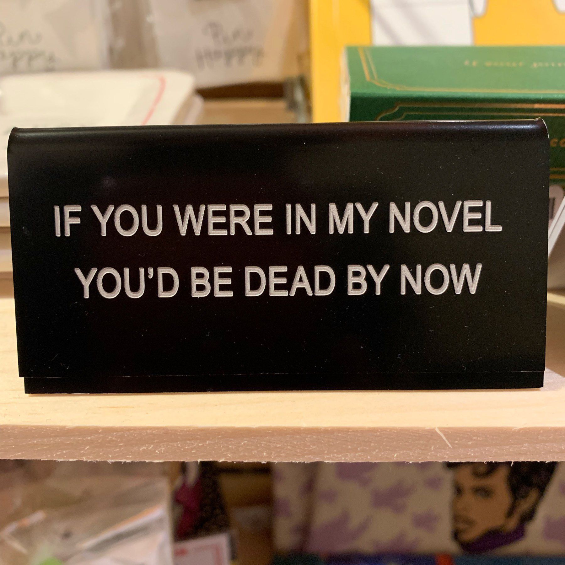Desk sign reading 'IF YOU WERE IN MY NOVEL YOU'D BE DEAD BY NOW'