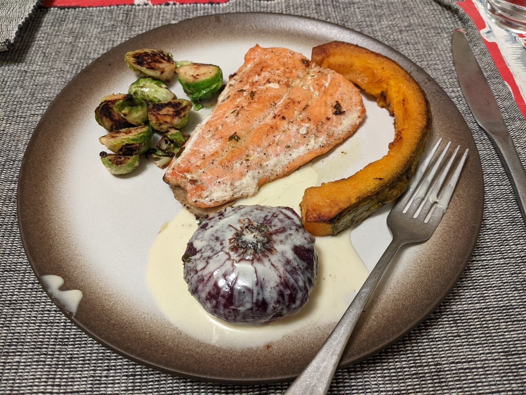 Plate of salmon, roasted squash wedge, whole roasted onion in cream sauce, and Brussels sprouts