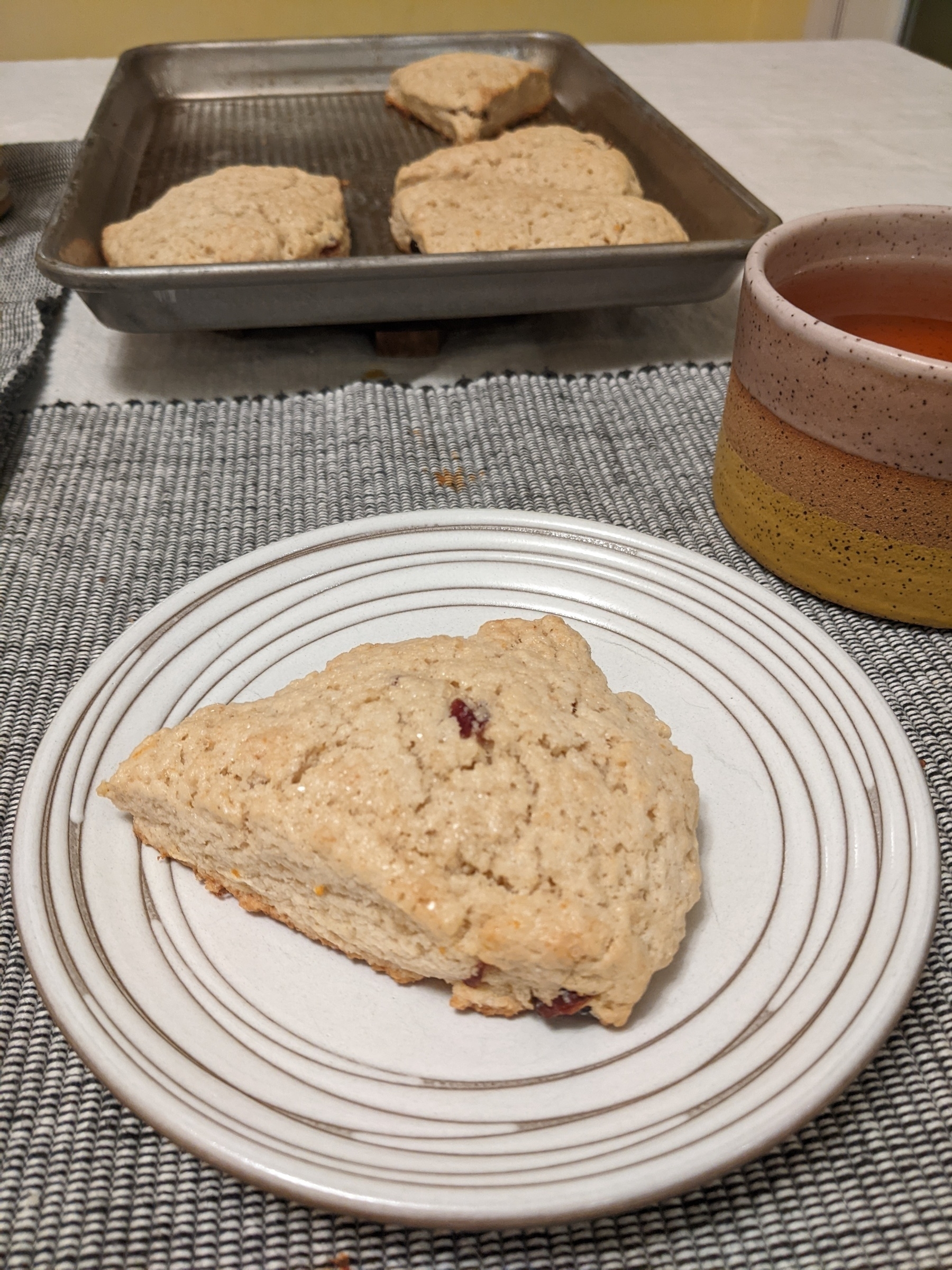 scone on small plate next to mug of tea and baking sheet with more scones 