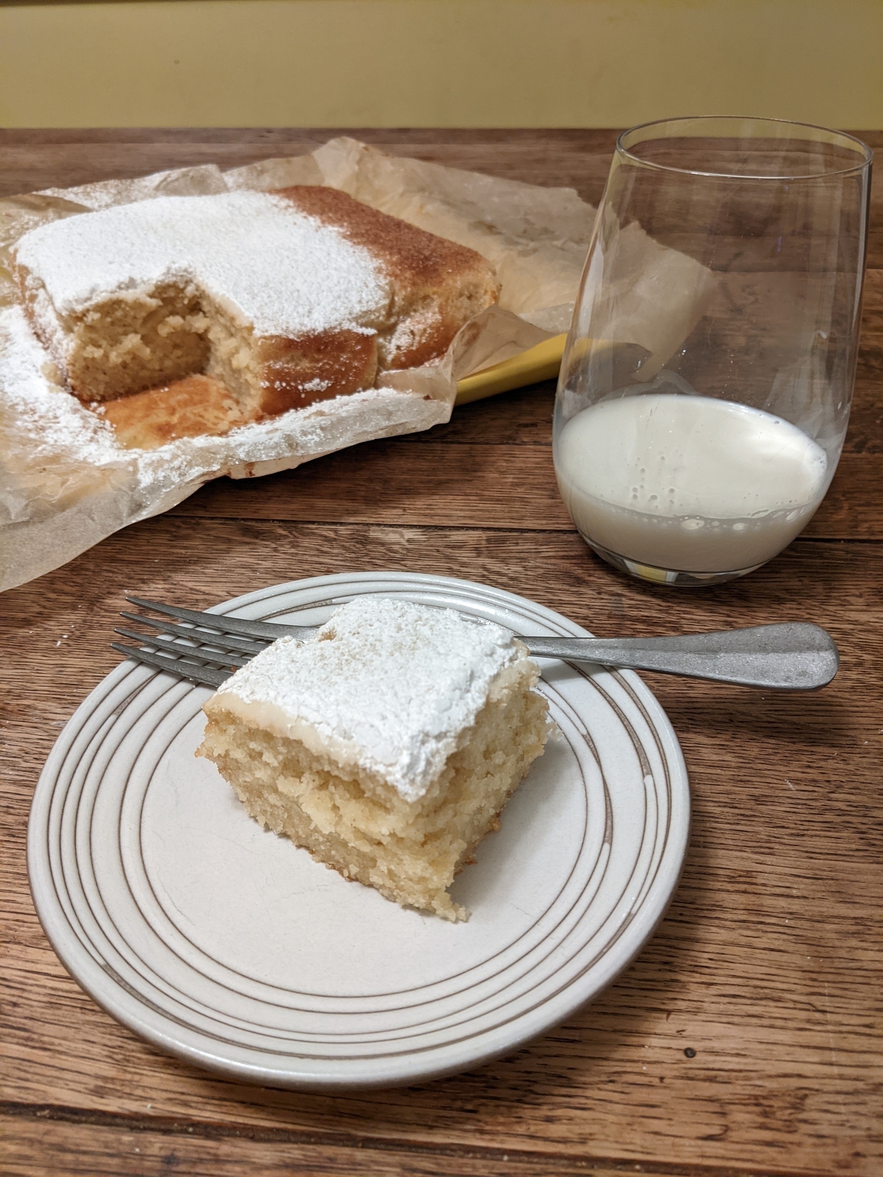 slice of yellow cake with powdered sugar topping beside square cake 